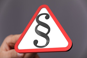 Hand holding a red triangle warning sign with a paragraph symbol.  Legal concept.