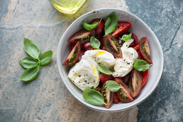 Caprese with heirloom tomatoes and torn buffalo mozzarella, horizontal shot on a beige and grey granite background, high angle view