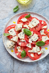 Sliced tomatoes with blue cheese and green basil, vertical shot on a blue and beige stone background, elevated view