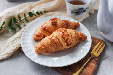 Two croissant in white plate with hot tea for morning breakfast or afternoon tea time