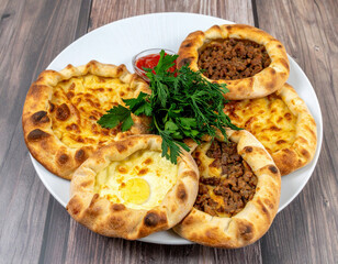 A white plate is beautifully arranged with a variety of Turkish pides filled with cheese, minced meat, and egg, garnished with fresh herbs and served with tomato sauce.