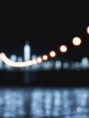 Warm glowing string lights with bokeh effect in front of blurred city skyline and dark cinematic night sky