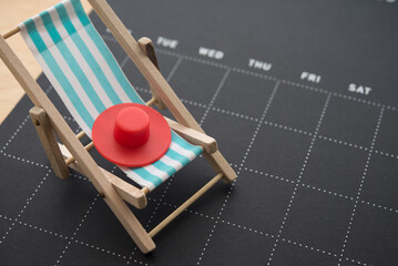Blue beach chair and red hat on black blank calendar background copy space. Annual leave travel...