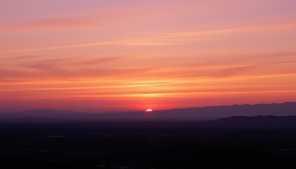 Naklejka premium Vibrant sunset over distant mountains and a hazy valley Orange and pink hues dominate the sky