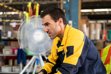 Tired adult male warehouse worker with light skin wearing yellow uniform jacket sitting and resting...