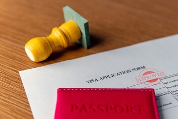 A visa application form with "APPROVED" stamp, a red passport, and a rubber stamp. International travel, permit, official consent concept.