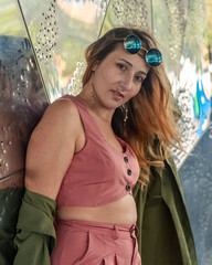 Plus size woman wearing pink outfit and trendy sunglasses leaning against metal wall