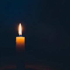 Fototapeta premium burning candle on black background. Single lit yellow candle on dark background with space for text.