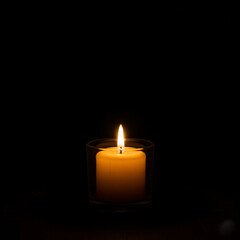 burning candle on black background. Single lit yellow candle on dark background with space for text.