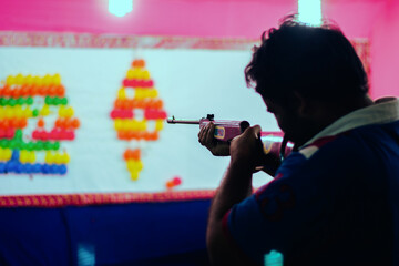 Closeup of a man holding rifle aiming at a shooting game booth.