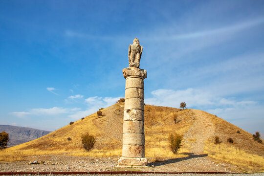 A majestic ancient eagle statue stands atop a tall stone column at Karakuş Tumulus, Adiyaman, Turkey. The historic site highlights rich cultural heritage under a clear blue sky.


