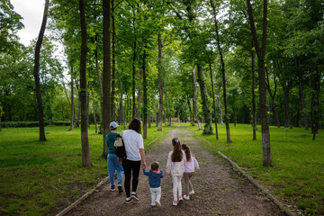 Fototapeta premium Family strolling through a lush green park surrounded by trees on a sunny day