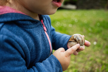 Child observing a snail in a natural grassy outdoor setting