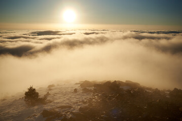 Sunrise over snow-covered mountain peak. Warm golden light of rising sun bathes clouds in soft hues...