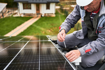 Man worker mounting photovoltaic solar panels on roof of house. Close up view of engineer installing solar module system with help of hex key. Concept of alternative, renewable energy.