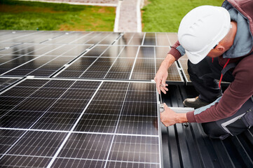 Man technician mounting photovoltaic solar panels on roof of house. Engineer in helmet installing solar module system with help of hex key. Concept of alternative, renewable energy.