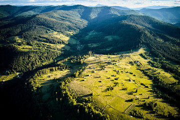 Aerial view of sunlit valley, dotted with small houses and winding roads, surrounded by dense...