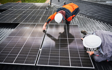 Professional technicians adjusting solar PV panels. Solar system installation on roof of house. Top view of two male workers in halmets and work overalls securing solar battery.