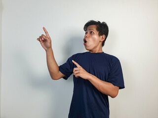 A young Asian man in a blue shirt looks surprised, pointing enthusiastically at something off-frame...