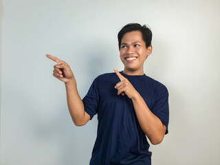 A young Asian man in a blue shirt looks surprised, pointing enthusiastically at something off-frame...