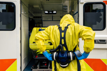 Member of biohazard team of emergency medical service in protective suit against ambulance.