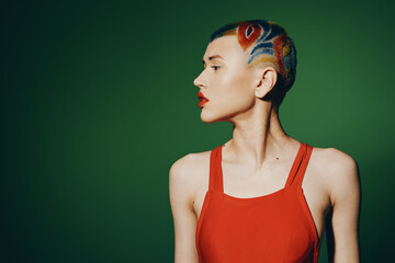 Creative woman with colorful shaved hair and red lipstick poses against a green background wearing...