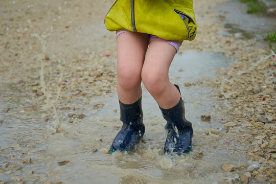 Jumping into a puddle close-up, boy's legs jumping into a puddle on a country road, rubber boots in the water