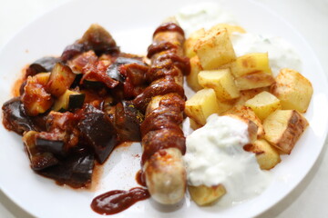 close-up of a currywurst with curry sauce, spanish potato cubes, tzatziki, eggplant, zucchini, tomato sauce