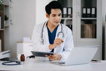 Doctor working on laptop and tablet and medical on clipboard on desk, electronics medical record...