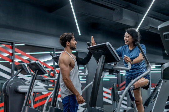 active middle aged woman person with prosthetic leg giving high five with trainer while exercise on gym equipment in fitness club - Powered by Adobe
