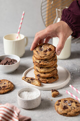 Woman taking homemade brown butter chocolate chip cookies with salt from plate at table. Selective focus.