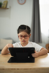Focused child wearing glasses engaged in tablet activities, showcasing concentration and learning in a modern home environment with natural light