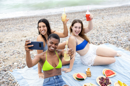 Cheerful multi-ethnic friends capturing a selfie together during a beach picnic