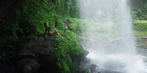 Woman Sitting Behind Waterfall in Jungle at Banyu Wana Amertha, Bali