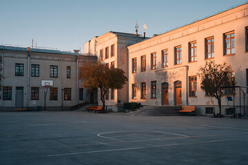 Schoolyard with basketball court and school building exterior in the sunny evening