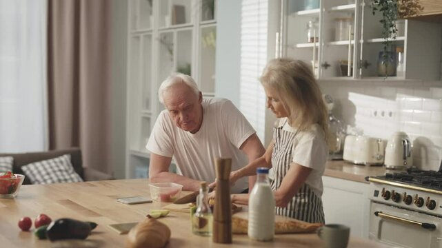 Calm sunday morning in home kitchen, old man and woman cooking breakfast. Happiness and joy of senior spouses, careful wife making snack-box for mature man, low-calories vegetables diet in old age