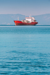 Red cargo ship sailing on calm blue sea with mountains in background, maritime transport concept