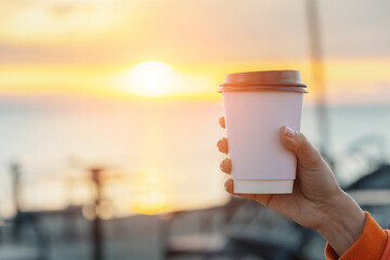 Woman savoring a moment of tranquility while holding a white takeaway coffee cup at sunrise by the sea, embracing the peaceful morning