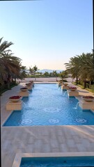 Infinity pool stretches toward horizon as sunlight dances across water surface, palm trees border calm area while resort reflects luxury, peace, and tropical rhythm near coastline.