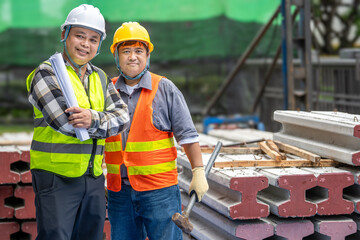 Two construction workers wea safety helmets and reflective vests standing outdoors at a...