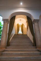 A grand staircase framed by ornate stone columns, green drapes, and a sparkling chandelier in a luxury boutique hotel's refined interior.