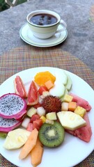 Tropical fruit medley spread on white ceramic plate, paired with steaming coffee mug, highlighting nutritious breakfast scene with natural morning lighting