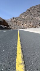Mountain road curves sharply toward rocky tunnel, mountain road lined with cracked stripe invites passage through rugged layers, contrast between built path and raw cliffs evokes timeless tension.