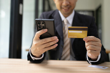 A man is using a laptop and a cell phone to pay for something. He is holding a credit card and a debit card
