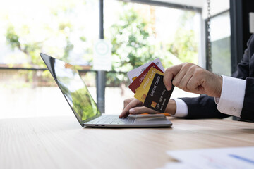 A man is using a laptop and a cell phone to pay for something. He is holding a credit card and a debit card
