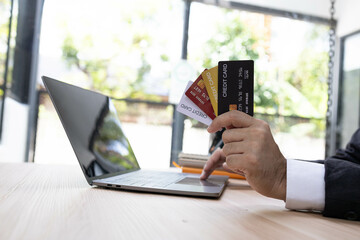 A man is using a laptop and a cell phone to pay for something. He is holding a credit card and a debit card
