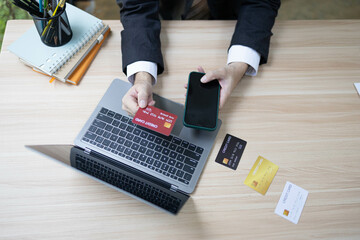 A man is using a laptop and a cell phone to pay for something. He is holding a credit card and a debit card
