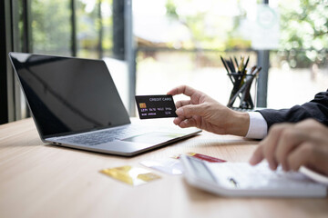 A man is using a laptop and a cell phone to pay for something. He is holding a credit card and a debit card
