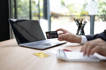 A man is using a laptop and a cell phone to pay for something. He is holding a credit card and a debit card
