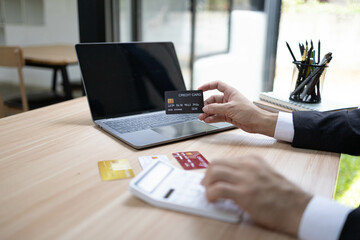 A man is using a laptop and a cell phone to pay for something. He is holding a credit card and a debit card
